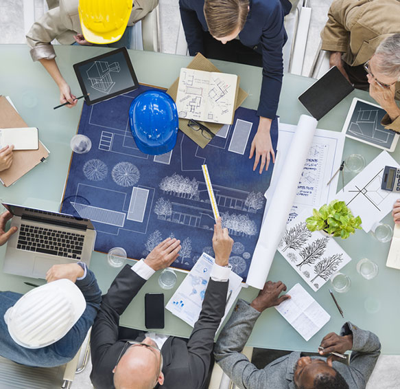 landscaping planning at table with group of professionals guy wearing a yellow hard hat looking at plans and sketches for developer services offered by neighborhood management