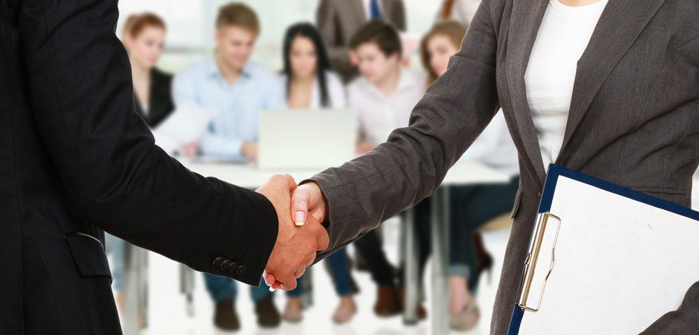 two business people shaking hands at a meeting with people watching them