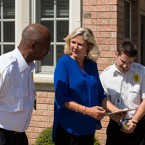 facility maintenace photo of woman in blue shirt with two men in uniform looking at clipboard outside of community center