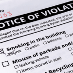 Close-up of a "Notice of Violation" ticket citing a building bylaw infraction, with "Smoking in the unit" marked as the offense.
