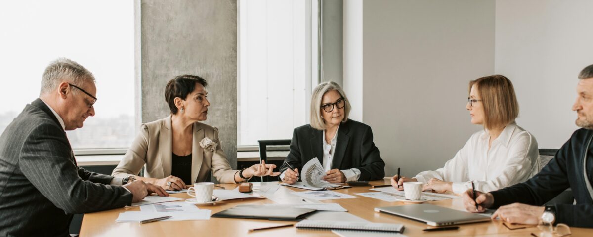 Board members discussing documents during a formal meeting around a conference table.