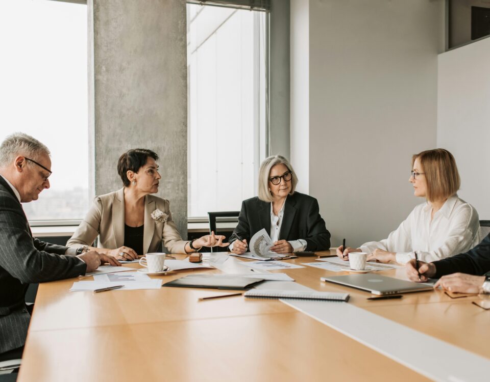 Board members discussing documents during a formal meeting around a conference table.