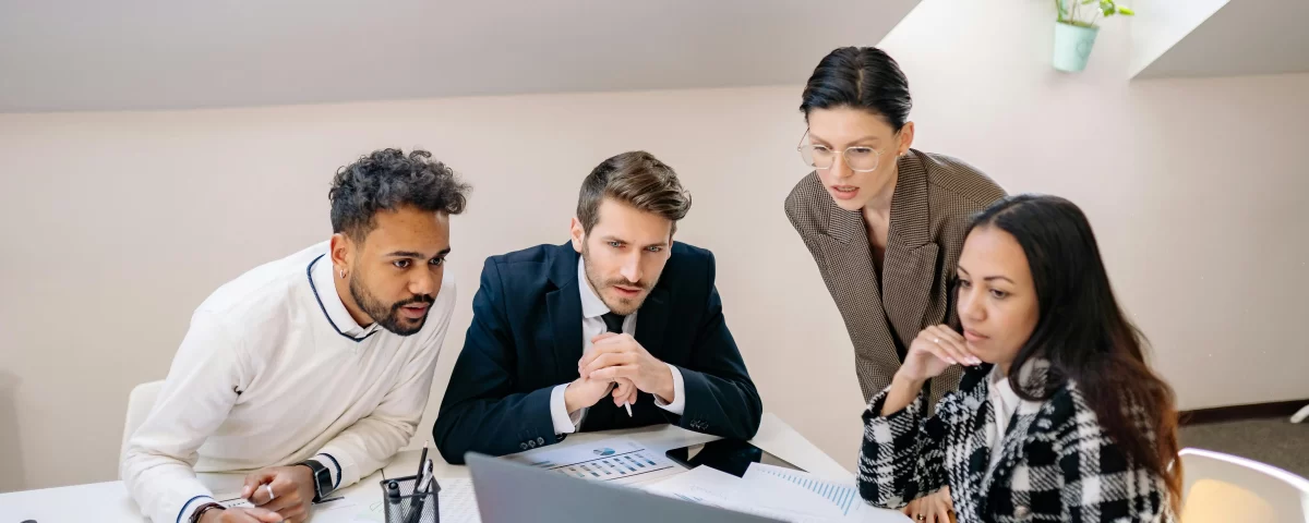 Team of professionals discussing transition plans while reviewing data on a laptop.