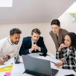 Team of professionals discussing transition plans while reviewing data on a laptop.