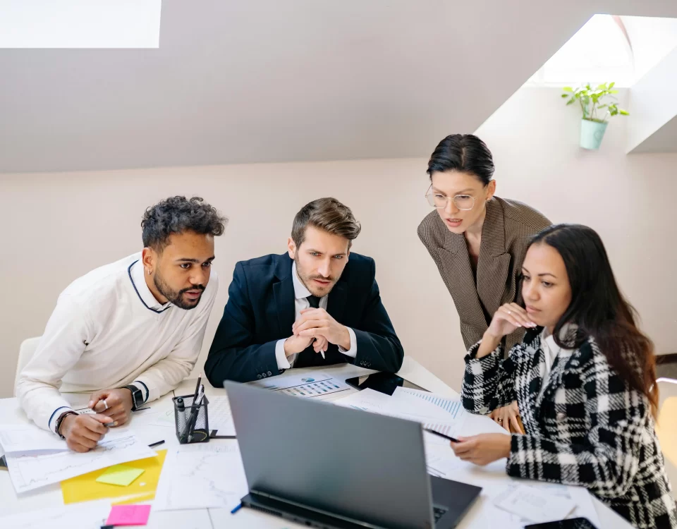 Team of professionals discussing transition plans while reviewing data on a laptop.